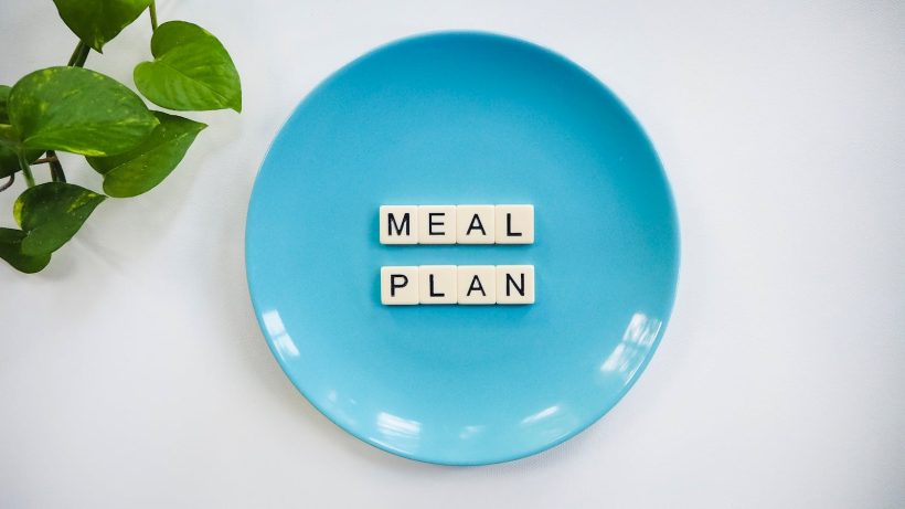 Innovative meal planning concept using alphabet tiles on a blue plate with green leaves.