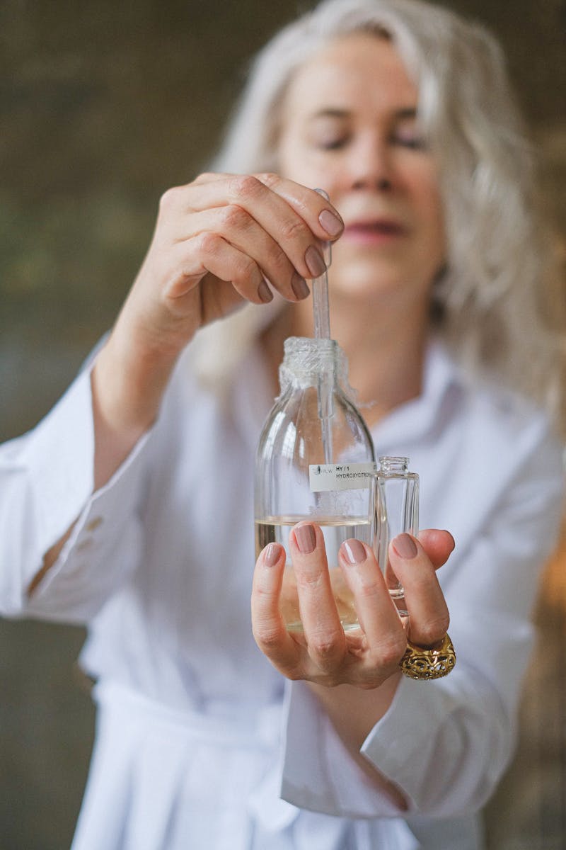 Close-up of a woman using a dropper to mix essential oils in a glass bottle indoors.