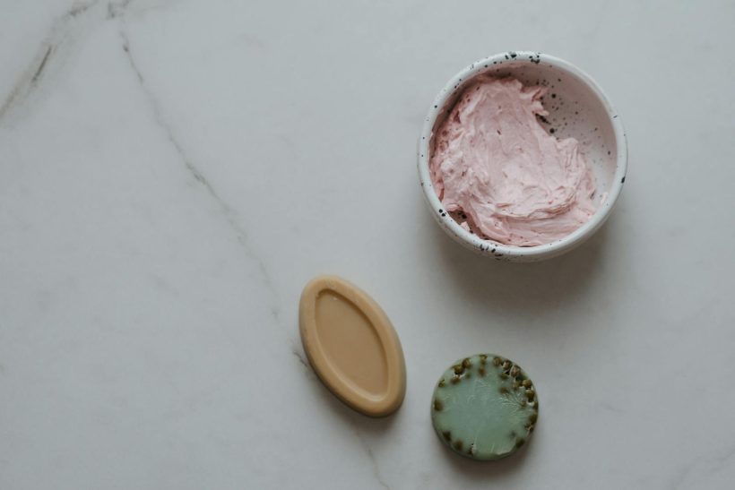 Top view of natural skincare products including soaps and cream on a marble background.