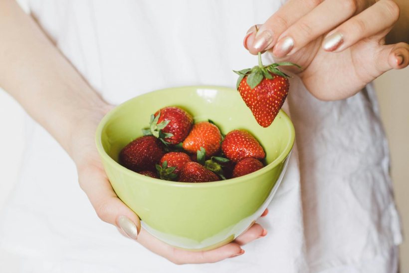 A close-up of a hand holding a green bowl filled with ripe strawberries, showcasing healthy lifestyle.