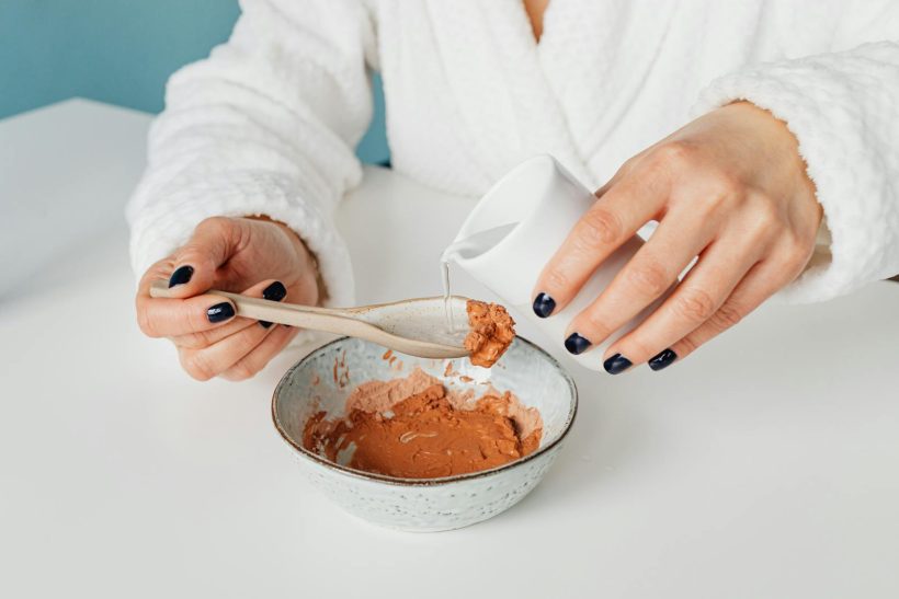 Close-up of a person mixing a natural clay mask with water for skincare.