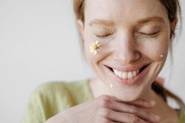 A cheerful woman with a chamomile flower on her cheek, eyes closed in a serene smile.